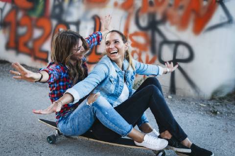 Two laughing friends sitting on longboard with arms outstretched model released Symbolfoto  HMEF00251