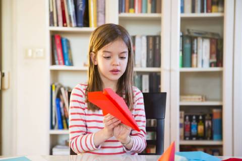 Girl tinkering paper plane on table at home model released Symbolfoto property released  LVF06860