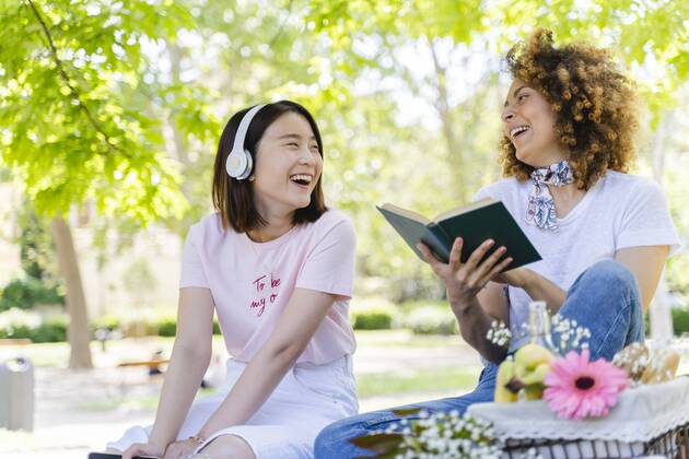 Two happy women with book and headphones relaxing in park model released Symbolfoto  FMOF00719