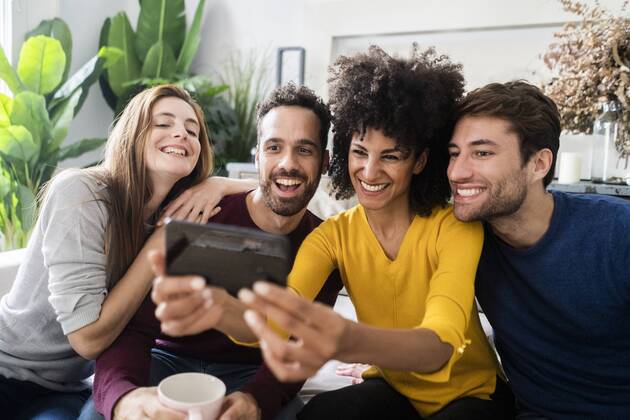 Four happy friends sitting on couch taking a selfie model released Symbolfoto property released  GIOF06442