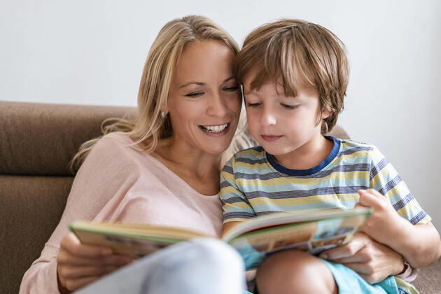 Mother and son reading a book together on couch at home model released Symbolfoto property released  DIGF08133