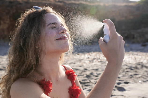 IMAGO Creative, Jahreszeit Sommer, Sonnenschutz Young woman applying suncream spray on the beach model released Symbolfoto  IGGF01320