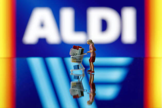 Eine Frau schiebt einen Einkaufswagen vor dem Logo des Konzerns Aldi