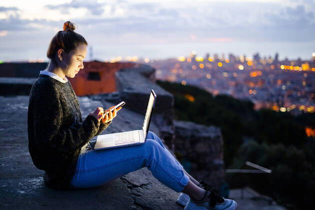 Young woman sitting on railing above the city using cell phone, Barcelona, Spain model released Symbolfoto GIOF07945