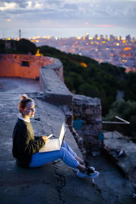 Young woman sitting on railing above the city using cell phone, Barcelona, Spain model released Symbolfoto GIOF07946
