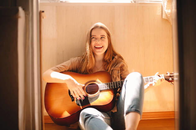 Creative Highlights Symbolfotos Cheerful young woman holding guitar while sitting on balcony floor ,model released, Symbolfoto CR_DMBE200115-273298-01