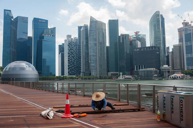 02.04.2020, Singapur, Republik Singapur, Asien - Ein Arbeiter repariert in Marina Bay Holzplanken entlang der Uferpromenade und der Skyline des Geschaeftsviertels im Hintergrund. Seit dem Ausbruch der Corona-Pandemie ist die Zahl auslaendischer Besucher komplett zurueck gegangen. Fuer gewoehnlich wimmelt die Gegend um Marina Bay Sands von Touristen, ist jetzt aber bis auf wenige Personen total verwaist.