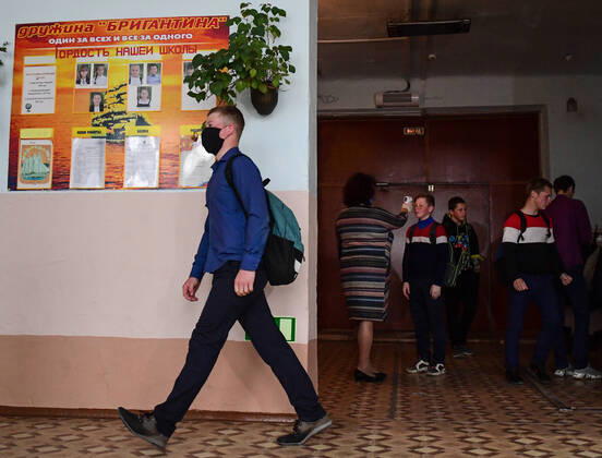 PRIMORYE TERRITORY, RUSSIA - APRIL 16, 2020: A pupil passes by as the headmistress checks other pupils temperature at the entrance to No 8 Comprehensive School in the village of Nezhino, some 40 km north of Vladivostok. After moving to online schooling due to the COVID-19 pandemic, educational institutions in the Primorye Territory are switching back to classroom teaching, with underfilled schools being the first to welcome pupils. Yuri Smityuk TASS  TS0D5F31