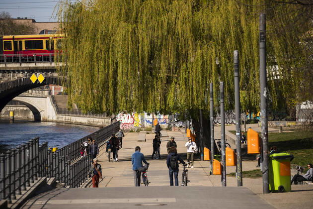 Menschen spazieren in der Sonne am Spreeufer in Berlin am 16. April 2020. Die von Bund und Laender um die Verbreitung des Coronavirus (SARS-CoV-2) zu verlangsamen beschlossenenen Massnahmen dauern auch vor der Ostertage weiter an. Die Debatte ueber eine Mundschutzpflicht und die Wirksamkeit der Masken dauert in der Oeffentlichkeit weiter an. Coronavirus in Berlin