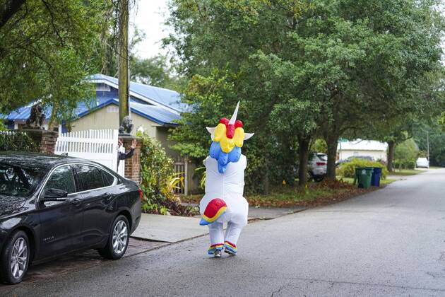 April 16, 2020, Tampa, Florida, USA: A neighbor peeks around his back gate as Corey Jurgensen, wearing an inflatable unicorn costume, runs by. Jurgensen has been wearing the costume during runs several times a week to cheer up others during this time of isolation but finds it therapeutic for herself as well to run through her Seminole Heights neighborhood wearing a silly costume. Tampa USA - ZUMAs70_ 20200416_zan_s70_039 Copyright: xMarthaxAsencioxRhinex
