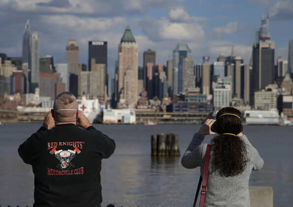 Pedestrians wearing protective face masks stop to photograph the Manhattan skyline while the USNS Comfort Navy ship remains docked at Pier 90 in Weehawken, NJ on Thursday, April 16, 2020. The USNS Comfort was originally designed to save lives in areas of war is now treating COVID-19 patients to help reduce the strain and pressure placed on the hospitals of New York City.  NYP20200416104 JOHNxANGELILLO
