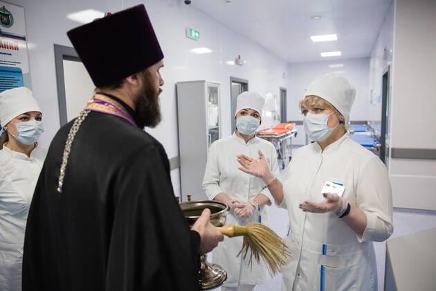 NIZHNY NOVGOROD, RUSSIA - APRIL 17, 2020: A Russian Orthodox priest talks to medical workers at a multipurpose medical centre for coronavirus patients constructed at army hospital No 422 of the Russian Defence Ministry; the Russian Defence Ministry is building 16 infectious disease centres for COVID-19 patients in various Russian cities; the centres under construction in Odintsovo, Podolsk, Volgograd, Novosibirsk, Orenburg, Ulan-Ude, and Ussuriysk are slated for completion by the end of April. Mikhail Solunin TASS  TS0D61B8