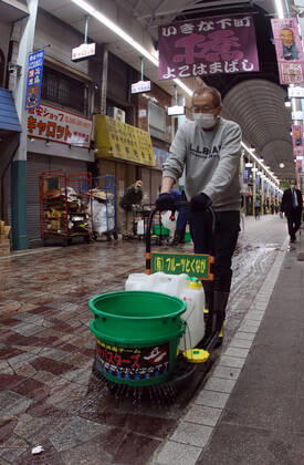 April 17, 2020, Yokohama, Japan - A member of Yokohamabashi shopping arcade trade association sprinkles disinfectant solution on the floor of their shopping arcade in Yokohama, suburban Tokyo on April 17, 2020. Japanese Prime Minister Shinzo Abe expanded a state of emergency across Japan to prevent outbreak of the new coronavirus.  (125464319)