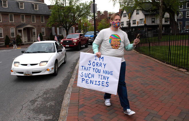 A counter protester demonstrates alongside vehicles participating in a car protest to reopen Maryland and end the stay at home order imposed during the Coronavirus COVID-19 pandemic, near the state capitol building in Annapolis, Maryland on Saturday, April 18, 2020. Drivers circled Annapolis hoking their horns and calling for Gov. Larry Hogan (R-MD) to end the stay at home order.  WAP20200418339 KEVINxDIETSCH