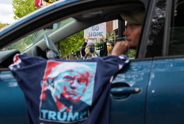 A counter protester holds a sign as a man drives past in his vehicle during a car protest to reopen Maryland and end the stay at home order imposed during the Coronavirus COVID-19 pandemic, near the state capitol building in Annapolis, Maryland on Saturday, April 18, 2020. Drivers circled Annapolis hoking their horns and calling for Gov. Larry Hogan (R-MD) to end the stay at home order.  WAP20200418345 KEVINxDIETSCH