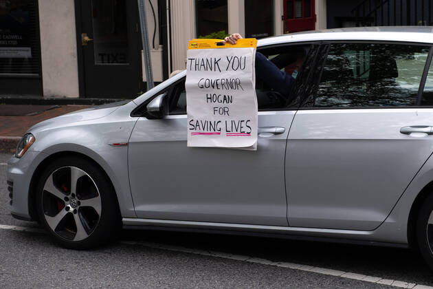 A counter protester holding a pro Gof. Hogan sign drives in a protest to reopen Maryland and end the stay at home order imposed during the Coronavirus COVID-19 pandemic, near the state capitol building in Annapolis, Maryland on Saturday, April 18, 2020. Drivers circled Annapolis hoking their horns and calling for Gov. Larry Hogan (R-MD) to end the stay at home order.  WAP20200418354 KEVINxDIETSCH