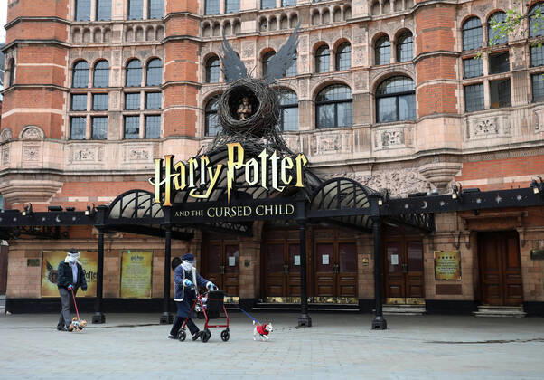 Day Twenty Six of Lockdown in London. A couple, in face masks and gloves, walk their dogs past the Palace Theatre which should have been showing Harry Potter and The Cursed Child. The country is on lockdown due to the COVID-19 Coronavirus pandemic. People are not allowed to leave home except for minimal food shopping, medical treatment, exercise - once a day, and essential work. COVID-19 Coronavirus lockdown, London, UK, on April 18, 2020 