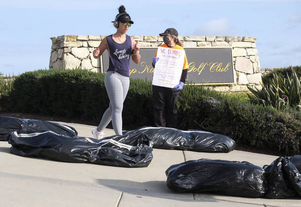 April 18, 2020, Los Angeles, California, U.S: A woman runs between demonstrators and fake body bags outside Trump National Golf Club Los Angeles in protest against U.S. President Donald Trump s response to the coronavirus disease (COVID-19) pandemic, in Rancho Palos Verdes, California, April 18, 2020. Los Angeles U.S. - ZUMAc68_ 20200418_zaf_c68_005 Copyright: xRingoxChiux