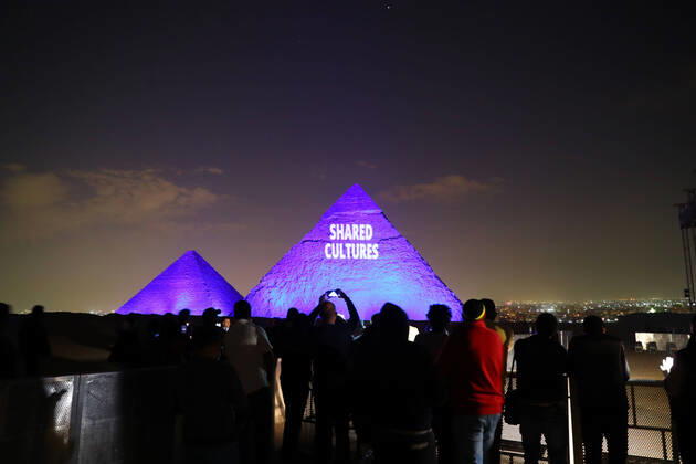 (200418) -- GIZA (EGYPT), April 18, 2020 (Xinhua) -- People gather near the Giza pyramids with one illuminated with words SHARED CULTURES during the World Heritage Day amid the COVID-19 pandemic in Giza, Egypt, on April 18, 2020. Egypt reported on Saturday 188 new COVID-19 cases, the highest daily increase, bringing the number of confirmed positive cases in the country to 3,032. (Xinhua Ahmed Gomaa) EGYPT-GIZA-PYRAMIDS-COVID-19-WORLD HERITAGE DAY-ILLUMINATION 
