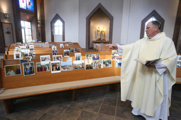 Rev. Bob Evans talks to photos of his parishioners during his Sunday service at the Holy Spirit Catholic Church in Maryland Heights, Missouri on Sunday, April 19, 2020. Since members cannot attend in person because of the Coronavirus pandemic, Evans asked for his church to send in photos of themselves receiving over 500 photos from his 1500 membership. The photos are taped to the pews where the family sits, while he preforms the weekly service via Facebook live.  SLP2020041907 BILLxGREENBLATT