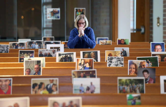 A church worker prays before a church service with photos of parishioners at the Holy Spirit Catholic Church in Maryland Heights, Missouri on Sunday, April 19, 2020. Since members cannot attend in person because of the Coronavirus pandemic, Rev. Bob Evans asked for his church to send in photos of themselves receiving over 500 photos from his 1500 membership. The photos are taped to the pews where the family sits, while he preforms the weekly service via Facebook live.  SLP2020041911 BILLxGREENBLATT