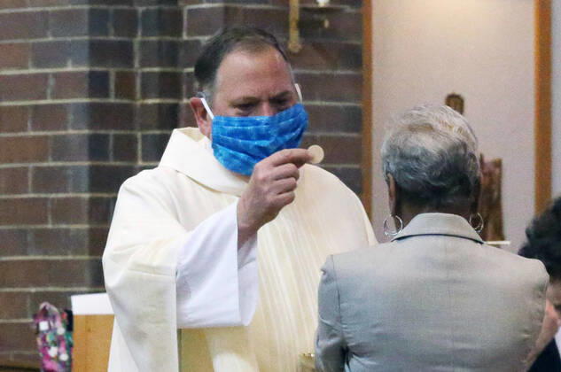 Rev. Bob Evans gives communion to one of three parishioners there to work his Sunday service at the Holy Spirit Catholic Church in Maryland Heights, Missouri on Sunday, April 19, 2020. Since members cannot attend in person because of the Coronavirus pandemic, Evans asked for his church to send in photos of themselves receiving over 500 photos from his 1500 membership. The photos are taped to the pews where the family sits, while he preforms the weekly service via Facebook live.  SLP2020041917 BILLxGREENBLATT