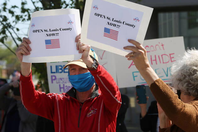 People wave signs as others sound their horns, driving by the St. Louis County Government Center, during a drive-by protest in Clayton, Missouri on Tuesday, April 21, 2020. The people driving around the block plus those with signs, cheering on the sidewalks are protesting the fact that Missouri businesses are closed due to the coronavirus pandemic.  SLP2020042107 BILLxGREENBLATT