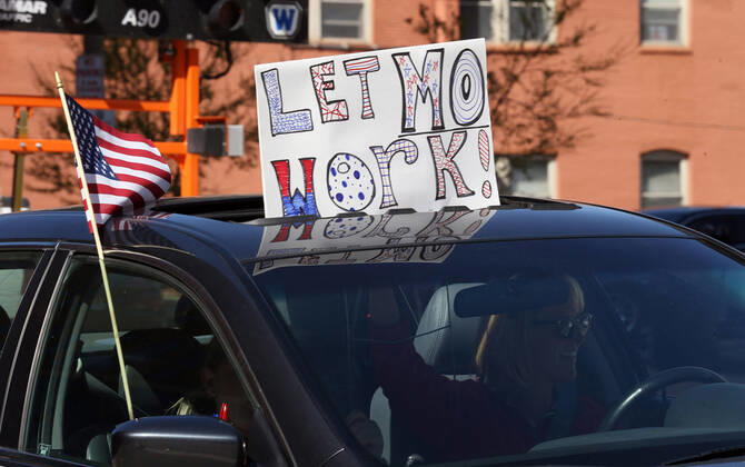 A woman holds a sign Let Mo Work! , while driving by the St. Louis County Government Center, during a drive-by protest in Clayton, Missouri on Tuesday, April 21, 2020. The people driving around the block, sounding their horns, plus those with signs, cheering on the sidewalks are protesting the fact that Missouri businesses are closed due to the coronavirus pandemic and want to return to work.  SLP2020042105 BILLxGREENBLATT