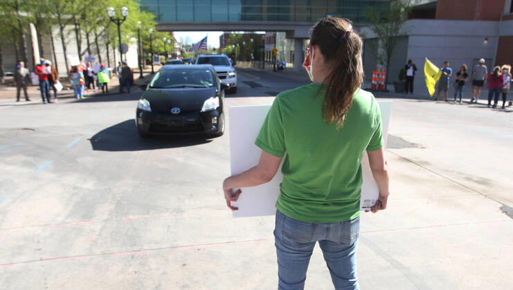 A protester stands in the street blocking traffic while others are driving by the St. Louis County Government Center, during a drive-by protest in Clayton, Missouri on Tuesday, April 21, 2020. The people driving around the block, sounding their horns, plus those with signs, cheering on the sidewalks are protesting the fact that Missouri businesses are closed due to the coronavirus pandemic and want to return to work.  SLP2020042106 BILLxGREENBLATT