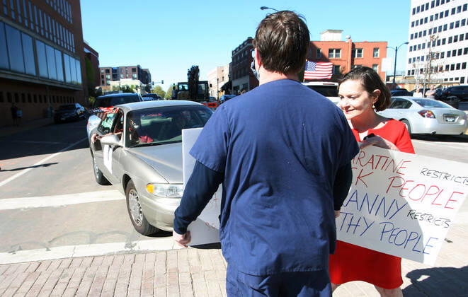 People with signs stand in the street, blocking those sounding their horns and driving by the St. Louis County Government Center, during a drive-by protest in Clayton, Missouri on Tuesday, April 21, 2020. The people driving around the block plus those with signs, cheering on the sidewalks are protesting the fact that Missouri businesses are closed due to the coronavirus pandemic.  SLP2020042110 BILLxGREENBLATT