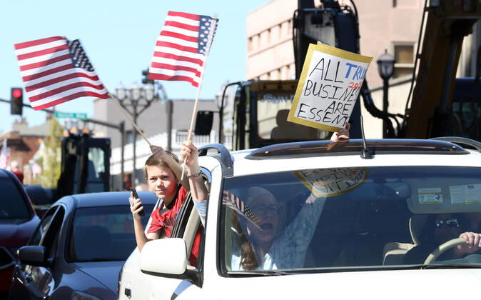 People wave American flags as they sound their horns, driving by the St. Louis County Government Center, during a drive-by protest in Clayton, Missouri on Tuesday, April 21, 2020. The people driving around the block plus those with signs, cheering on the sidewalks are protesting the fact that Missouri businesses are closed due to the coronavirus pandemic.  SLP2020042111 BILLxGREENBLATT