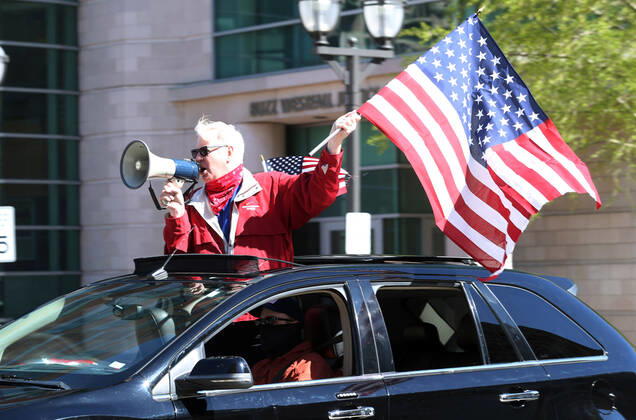 People wave American flags as they sound their horns, driving by the St. Louis County Government Center, during a drive-by protest in Clayton, Missouri on Tuesday, April 21, 2020. The people driving around the block plus those with signs, cheering on the sidewalks are protesting the fact that Missouri businesses are closed due to the coronavirus pandemic.  SLP2020042113 BILLxGREENBLATT