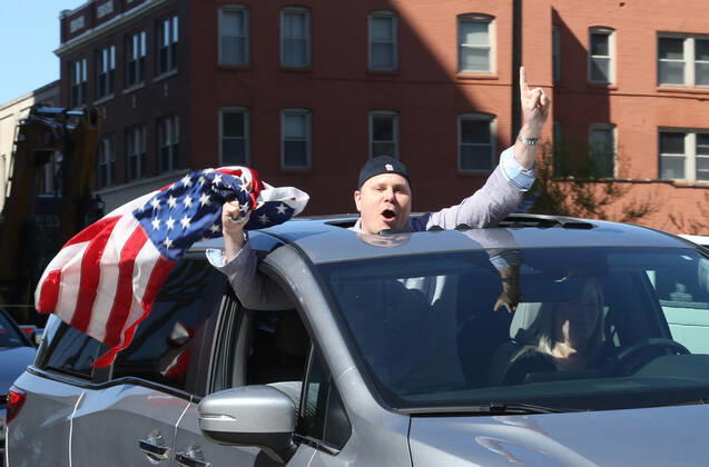 People wave American flags as they sound their horns, driving by the St. Louis County Government Center, during a drive-by protest in Clayton, Missouri on Tuesday, April 21, 2020. The people driving around the block plus those with signs, cheering on the sidewalks are protesting the fact that Missouri businesses are closed due to the coronavirus pandemic.  SLP2020042114 BILLxGREENBLATT