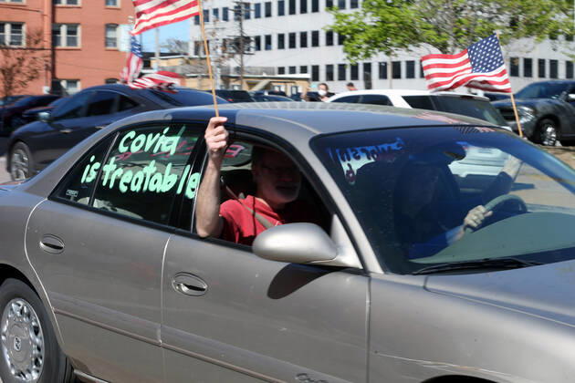 People wave American flags as they sound their horns, driving by the St. Louis County Government Center, during a drive-by protest in Clayton, Missouri on Tuesday, April 21, 2020. The people driving around the block plus those with signs, cheering on the sidewalks are protesting the fact that Missouri businesses are closed due to the coronavirus pandemic.  SLP2020042115 BILLxGREENBLATT