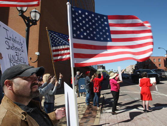 People wave American flags watching drivers pass the St. Louis County Government Center, during a drive-by protest in Clayton, Missouri on Tuesday, April 21, 2020. The people driving around the block plus those with signs, cheering on the sidewalks are protesting the fact that Missouri businesses are closed due to the coronavirus pandemic.  SLP2020042116 BILLxGREENBLATT