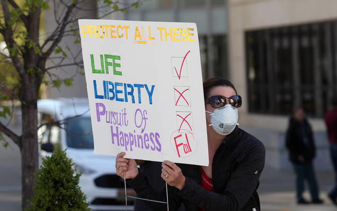 A woman waves her sign as others drive by the St. Louis County Government Center, during a drive-by protest in Clayton, Missouri on Tuesday, April 21, 2020. The people driving around the block plus those with signs, cheering on the sidewalks are protesting the fact that Missouri businesses are closed due to the coronavirus pandemic.  SLP2020042117 BILLxGREENBLATT