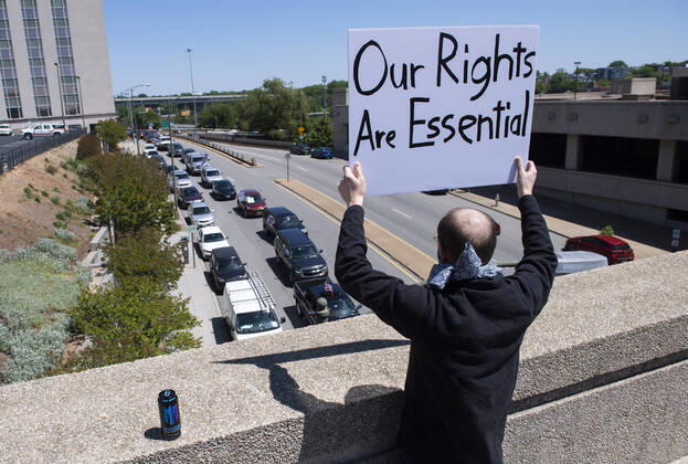A man holds a sign from an overpass as protesters demonstrate from the vehicles below as they call on Gov. Ralph Northam to reopen Virginia and end executive order 53 with bans gatherings of over 10 in the midst of the Coronavirus COVID-19 pandemic, near the State Capitol Building in Richmond, Virginia on Wednesday, April 22, 2020. The group is urging the reopening of business despite the COVID-19 pandemic still infecting the nation.  WAP20200422305 KEVINxDIETSCH