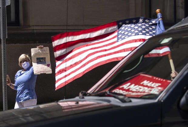 A self-identified member of the medical community holds a counter protest as demonstrators protest from the vehicles as they call on Gov. Ralph Northam to reopen Virginia and end executive order 53 with bans gatherings of over 10 in the midst of the Coronavirus COVID-19 pandemic, near the State Capitol Building in Richmond, Virginia on Wednesday, April 22, 2020. The group is urging the reopening of business despite the COVID-19 pandemic still infecting the nation.  WAP20200422315 KEVINxDIETSCH