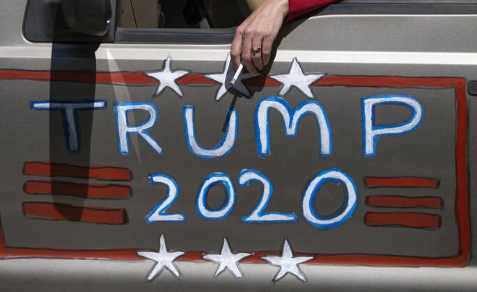 A protesters smokes alongside a Trump 2020 sign as they demonstrate calling on Gov. Ralph Northam to reopen Virginia and end executive order 53 with bans gatherings of over 10 in the midst of the Coronavirus COVID-19 pandemic, near the State Capitol Building in Richmond, Virginia on Wednesday, April 22, 2020. The group is urging the reopening of business despite the COVID-19 pandemic still infecting the nation.  WAP20200422320 KEVINxDIETSCH