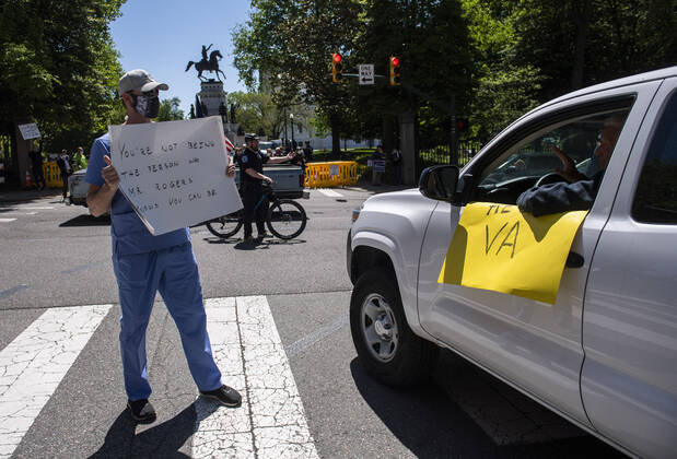 A counter protester in medical scrubs demonstrates as Reopen Virginia protesters participate in a car rally calling on Gov. Ralph Northam to reopen Virginia and end executive order 53 with bans gatherings of over 10 in the midst of the Coronavirus COVID-19 pandemic, near the State Capitol Building in Richmond, Virginia on Wednesday, April 22, 2020. The group is urging the reopening of business despite the COVID-19 pandemic still infecting the nation.  WAP20200422328 KEVINxDIETSCH