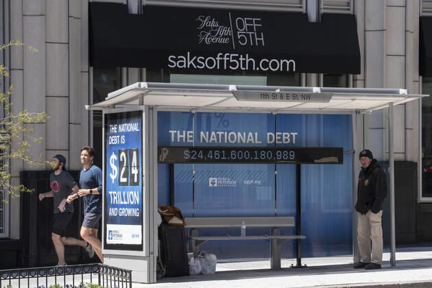 A homeless man takes shelter at a bus stop that displays a running total of the national debt on 11th street in downtown Washington, DC during the normal business lunch hour on Wednesday, April 22, 2020. Office buildings, retail stores and restaurants are essentially closed downtown in the Nation s Capital due to COVID-19. Depending on how long the shutdown will last, some say 30% to 50% of the DC restaurants and bars will not be able to reopen.  WAS20200422051 PATxBENIC