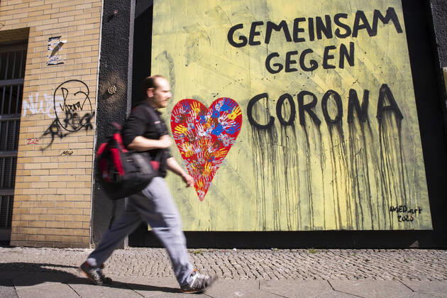Mann laeuft vor einem Grafitti Gemeinsam gegen Corona in Berlin am 22. April 2020. Ab heute koennen in Berlin laeden unter 800 qm, Buchhandlucngen und Autosalons wieder oeffnen mit Einhanltung von Hygiene und Distanzvorschriften. Coronavirus in Berlin