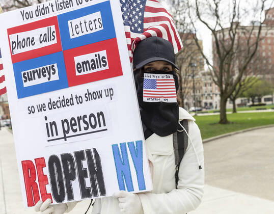 NY: Operation Gridlock in Albany A woman wearing facial mask made as American flag and holding poster participates in Operation Gridlock protest outside of New York State Capitol Building. Participants demanded reopening of New York State. Many people on the street disregarded wearing facial masks and keep social distances. Albany New York United States Copyright: LevxRadin