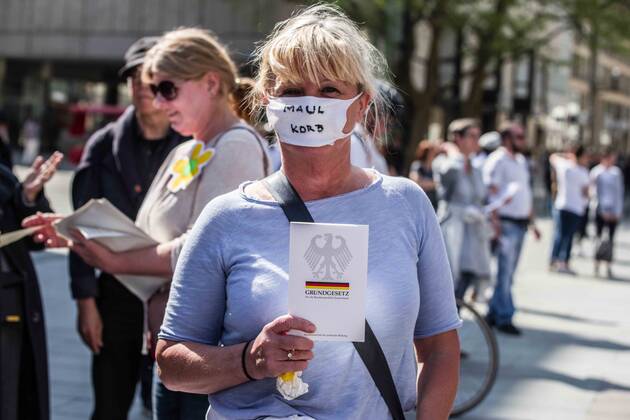 April 25, 2020, Munich, Bavaria, Germany: Muzzle written on a mask while holding a copy of the German Bill of Rights at a QAnon-like demo in Munich, Germany. Organized in Telegram chats by conspiratorial â€oeQuerfront†(cross-front) groups, the city of Munich, Germany saw numerous anti-state â€oeCorona Parties†as under mottos such as â€oeDemonstration fuer die Erhaltung der Grundrechte†(Demonstration for the Upholding of Basic Rights) and â€oeFuer unsere Freiheit, unsere Grundrechte und unsere Selbstbestimmung†(Demonstration for our Freedom, Basic Rights, and Self-Determination). Numerous right-extremists, Verfassungsschutz-monitored figures, QAnon fans, and AfD politicians were in attendance. The groups are of the belief that the anti-Coronavirus measures are power-grabs. Querfront groups a - ZUMAb160 20200425_zbp_b160_030 Copyright: xSachellexBabbarx