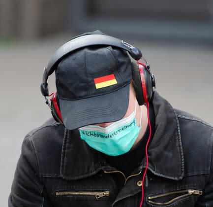 Lockdown beenden sofort! - Demonstration auf dem Südermarkt von Flensburg Die Kommunikationsstelle Demokratischer Widerstand veranstaltet eine Demonstration am 25.04.2020 in Flensburg auf dem Südermarkt, Innenstadt; Demonstrant mit Maske und Köpfhörer auf, trägt Maske wo geschrieben steht ich bin anderer Meinung , er sitzt auf dem Boden, hält Lektüre in der Hand (Grundgesetz)