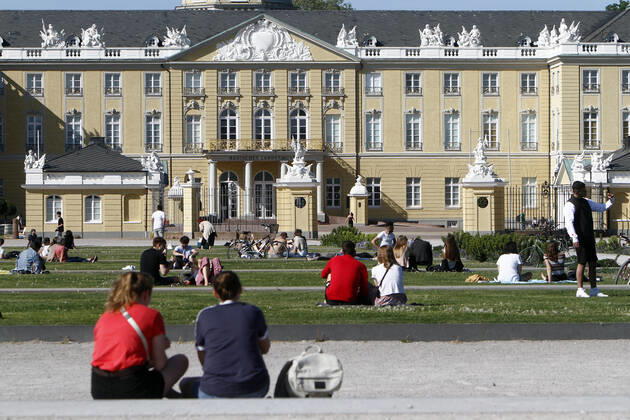 Personen sitzen unter Achtung der Abstandsregeln auf den Rasenflächen am Schlossplatz vor dem Landesmuseum und Schloss und genießen den warmen Frühlingstag in der Innenstadt von Karlsruhe, r Innenstadt von Karlsruhe, Baden Württemberg, Deutschland