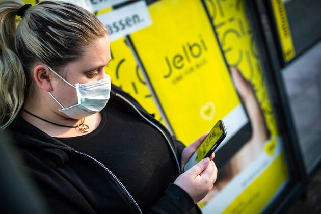 Ein Frau mit einer Mund-Nasen-Maske nutzt die BVG -App auf ihrem Smartphone an einer Bushaltestelle der BVG in Berlin. Ab Montag, den 27. April 2020 gilt eine Maskenpflicht im ÖPNV. Maskenpflicht im ÖPNV