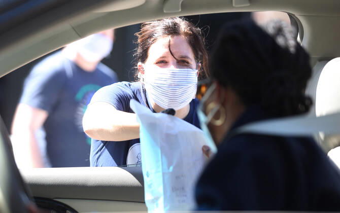 A volunteer hands off a bag of prepared sandwiches, to one of many that have waited in their cars for free food, in St. Louis on Sunday, April 26, 2020. Hundreds of cars lined the streets for an opportunity to receive food from several restaurants, while the group took donations for theThe Gateway Resilience Fund, an organization that assists fellow restaurant workers that are out of work because of the coronavirus.  SLP2020042601 BILLxGREENBLATT