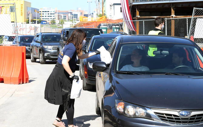 A volunteer hands off a bag of prepared sandwiches, to one of many that have waited in their cars for free food, in St. Louis on Sunday, April 26, 2020. Hundreds of cars lined the streets for an opportunity to receive food from several restaurants, while the group took donations for the The Gateway Resilience Fund, an organization that assists fellow restaurant workers that are out of work because of the coronavirus.  SLP2020042602 BILLxGREENBLATT