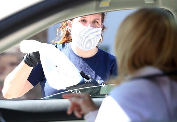 A volunteer hands off a bag of prepared sandwiches, to one of many that have waited in their cars for free food, in St. Louis on Sunday, April 26, 2020. Hundreds of cars lined the streets for an opportunity to receive food from several restaurants, while the group took donations for theThe Gateway Resilience Fund, an organization that assists fellow restaurant workers that are out of work because of the coronavirus.  SLP2020042603 BILLxGREENBLATT